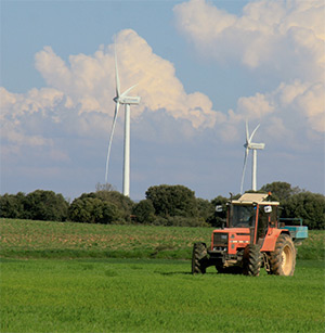 Un tractor trabaja en un campo junto a unos molinos de viento